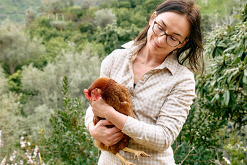 Woman holding brown hen in her hands in the farm. Free-grazing domestic hen on a traditional free range poultry organic farm.