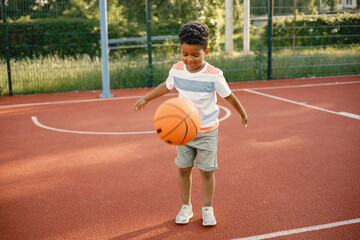 Obraz premium Multiracial boy standing on a basketball court and play with an orange ball