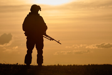 Military soldier silhouette with machine gun over sunset