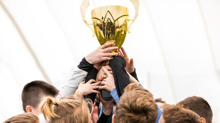 Happy kids winning sports tournament. Schoolboys standing in a circle and holding the golden...