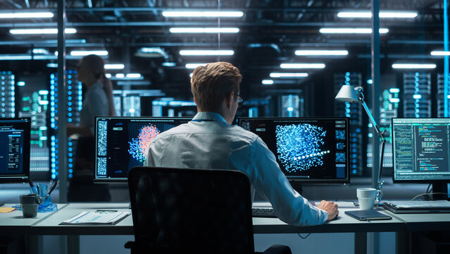 In the Futuristic Laboratory or Office Male Scientists Working at the Two Monitors. Developer Writing Code at the Evening. Computer Engineer Create Neural Network at His Workstation
