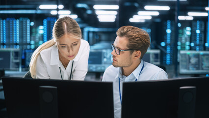 IT Specialist Works on Two Personal Computer at the Software Program with Coding Language Interface. In the Background Technical Room of Data Center with Professional Working