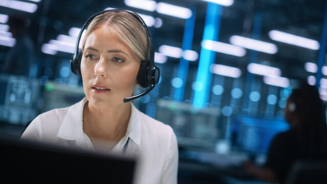 Beautiful Caucasian Female Call Center Operator In Headsets Working In Office And Looking At The Two Monitors. Call Center, Telemarketing, Customer Support Agent Provide Service On Conference Call