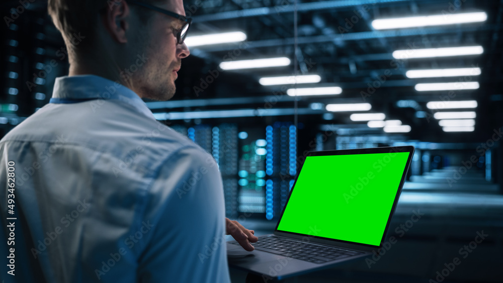 Poster View Over the Shoulder of Male IT Specialist Using Laptop Computer in Data Center, Looking at the Screen. Successful Businessman and e-Business Entrepreneur Working Alone. Innovation Concept