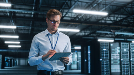 Young Caucasian Male Employee Uses Tablet Computer in System Control Monitoring Center at Night. Evening Office In the Background. Cyber Security and Network Protection Concept