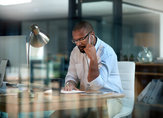 I need to work smart with this goal, not harder. Cropped shot of a mature businessman sitting in his office at night and looking contemplative while wearing earphones.