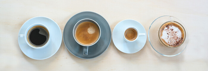 Four cups with various coffee, espresso, cappuccino, lungo, black and with crema on a light wooden table, panoramic format, copy space, high angle view from above
