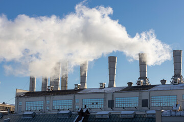 Boiler room with fuming pipes pipes against the blue sky.
