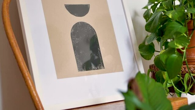 Geometric framed art on a kraft brown paper on wood chair with plant, in a home lifestyle setting