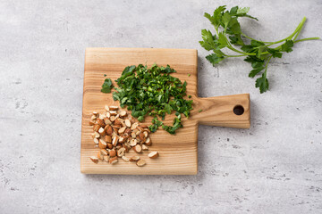 Wooden board with chopped almonds and parsley on a light gray textured background, top view