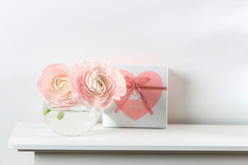 Three pale pink ranunculus in a transparent round vase on the white windowsill. Copy space. Place for text
