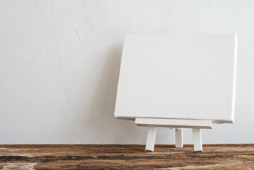 Blank white wooden easel canvas on wooden table with white wall background copy space. Creative...