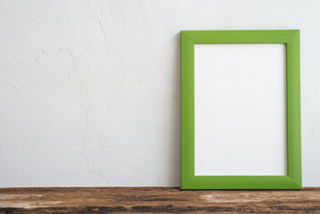 Empty green photo frame on old wooden table over white wall background copy space. Home decoration, creative idea design concept.