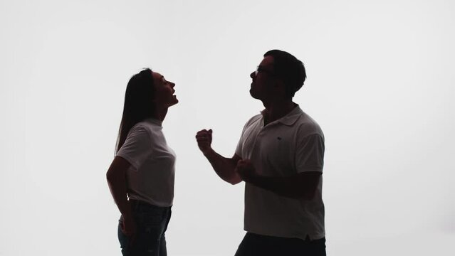 Silhouette of man who threatens woman that will hit her, she stands confidently and is not afraid of him, white background in studio, side view. Concept confidence and bravery