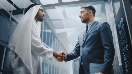 Businessman Talking with Arab Investment Partner while Riding Glass Elevator to Office in a Modern...