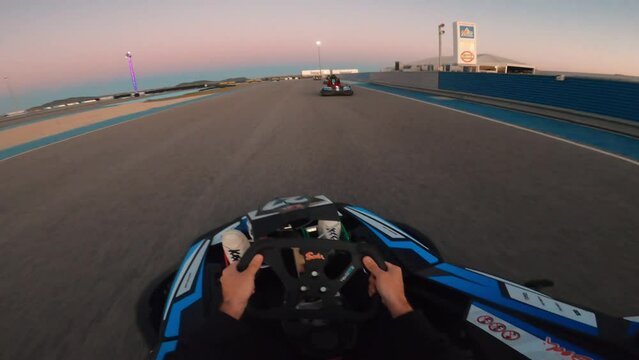 Point of view man driving a kart outdoor at sunset. Racers driving karts on a race track. First person view of steering a go cart while racing in a fun competition