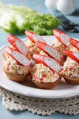 Tartlets with crab sticks, eggs, cheese and cucumber on a plate on blue background. Festive snack. Close-up