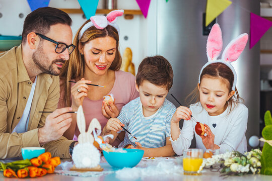 Lovely family prepare for Easter at domestic kitchen. Mother, father, son and daughters are painting eggs. Happy family are preparing for Easter. Cute little child girl and boy wearing bunny ears.