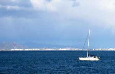 Obraz premium Sailboat at sea on sailing on the waves. Yachtsman during training on a sailboat. Skiff and Sailboat in sea port near the Spanish coast. Sail sport in Yacht club. Sail boat on waves on sunset in sea.