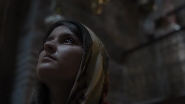 Young woman in traditional clothes looking up, while standing inside the church. Slow motion.