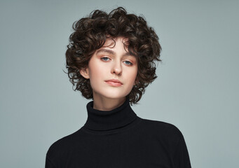 Portrait of brunette with curls wear high neck jumper isolated on grey background
