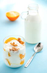 Obraz na płótnie Canvas Greek yogurt with orange and walnuts in glasses on a blue table. Healthy food. Health eating concept. Selective focus.