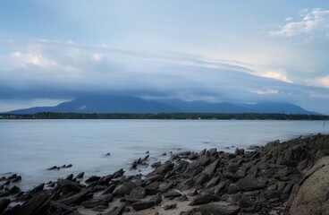 potrait of a rocky beach calm water and cloudy mountain
