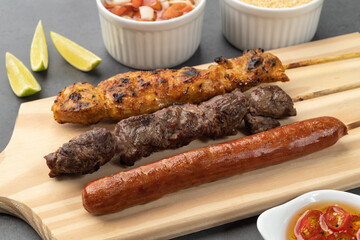Meat, chicken and pork sausage skewers over wooden board with farofa and vinaigrette