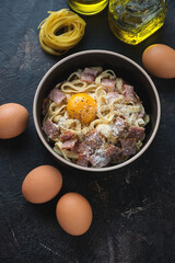 Bowl with italian pasta carbonara on a dark-brown stone background, vertical shot, elevated view