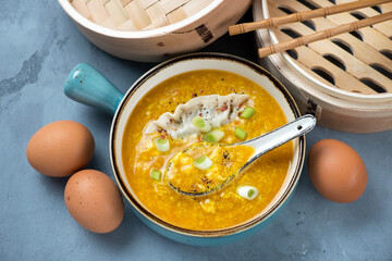 Bowl of chinese traditional egg-drop soup served with dumpling, elevated view on a grey concrete background, horizontal shot