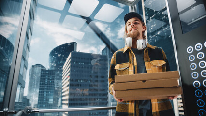 Young Handsome Specialist Riding Glass Elevator in Modern Office Building. Restaurant Delivery Courier Holding Take Away Pizza Boxes. Handsome Employee Bringing Fast Food to Business Office.
