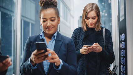 Two Diverse Multiethnic International People Ride a Glass Elevator to Office in a Modern Business Center. Focus on Different Businesspeople Using Smartphones in a Lift.