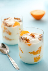 Greek yogurt with orange and walnuts in glasses on a blue table. Healthy food. Health eating concept. Selective focus.