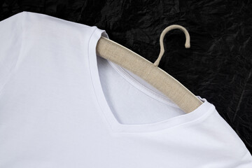 Mock-up of a white cotton T-shirt, on a linen hanger. Close-up, black background