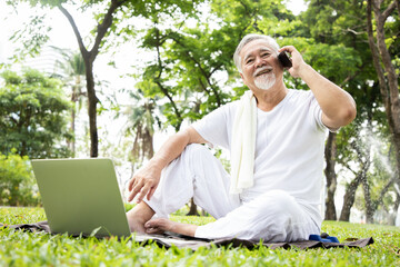 Obraz premium Elderly Asian man relaxing and talking with friends after yoga session in computer laptop. Concept of staying healthy and living after retirement. Meditation in park concept