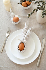 Rustic Easter table setting. Easter egg in Easter bunny napkin on plate on linen tablecloth. Easter...