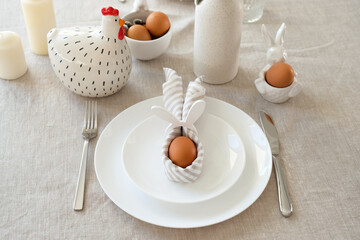 Cute Easter table setting. Easter egg in Easter bunny napkin on plate on linen tablecloth.
