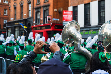 Fototapeta na wymiar Person taking photos of the march, green hats in the crowd, the Saint Patrick's day parade in Dublin 2022, Ireland
