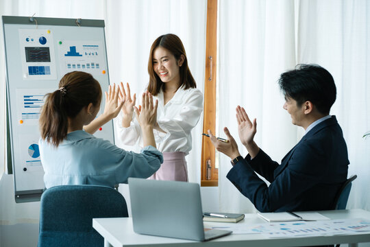 Happy diverse Asian employees coworkers or business partners joining hands in high five gesture celebrating success or victory, feeling motivated.