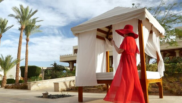 Summer vacation woman in red hat and cape for the beach with mobile phone near gazebo and palms, woman blogger,