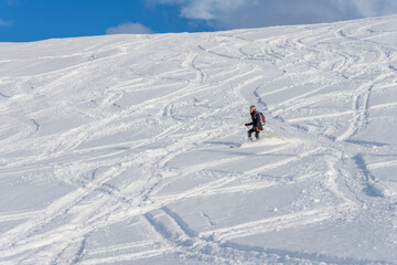 Woman with brown hair, wearing ski wear and a bagpack skiing down a beautiful snow hill with plenty...