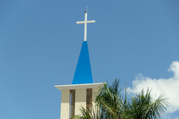 Topo de igreja com um crucifixo branco contra o céu azul. Igreja Nossa Senhora de Aparecida em Goiânia.
