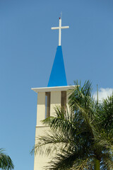 Topo de igreja com um crucifixo branco contra o céu azul. Igreja Nossa Senhora de Aparecida em Goiânia.