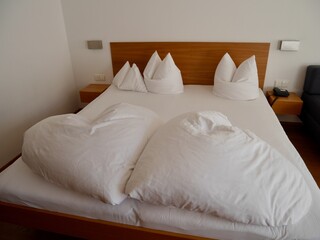 Close up of wooden bed with heart-shaped white cushions in modern minimalist bedroom.