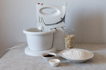 The process of making American oatmeal cookies. Mixer for mixing ingredients, oatmeal, flour, chocolate drops, baking powder on the table. Recipe. Article. Cooking.