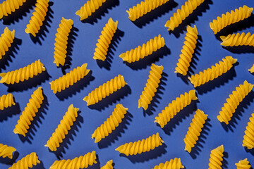 Dried spiral Italian pasta scattered on a blue background