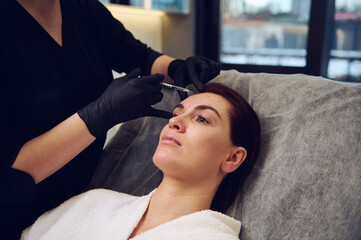 Close-up cosmetologist beautician aesthetician injecting a botulinum toxin injection in the forehead of middle aged European woman in wellness spa clinic for rejuvenating anti-aging therapy