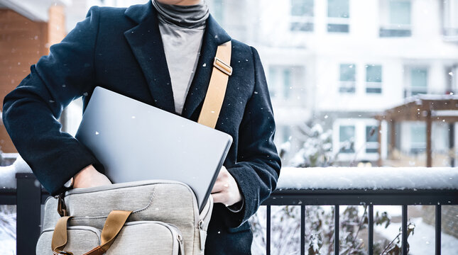 Business people wearing black coat put laptop in the suitcase after work with snow falling, standing outside the buildings. Freelance job, remote worker concept. Crop image of businessman outdoor.