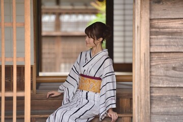 日本家屋の玄関先に座る若く美しい浴衣を着た女性