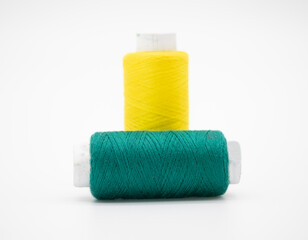 Sewing thread and bobbin in Dark Cyan and yellow on isolated white background